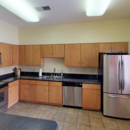 A dated kitchen in a leasing clubhouse, with fluorescent lighting and industrial cabinets